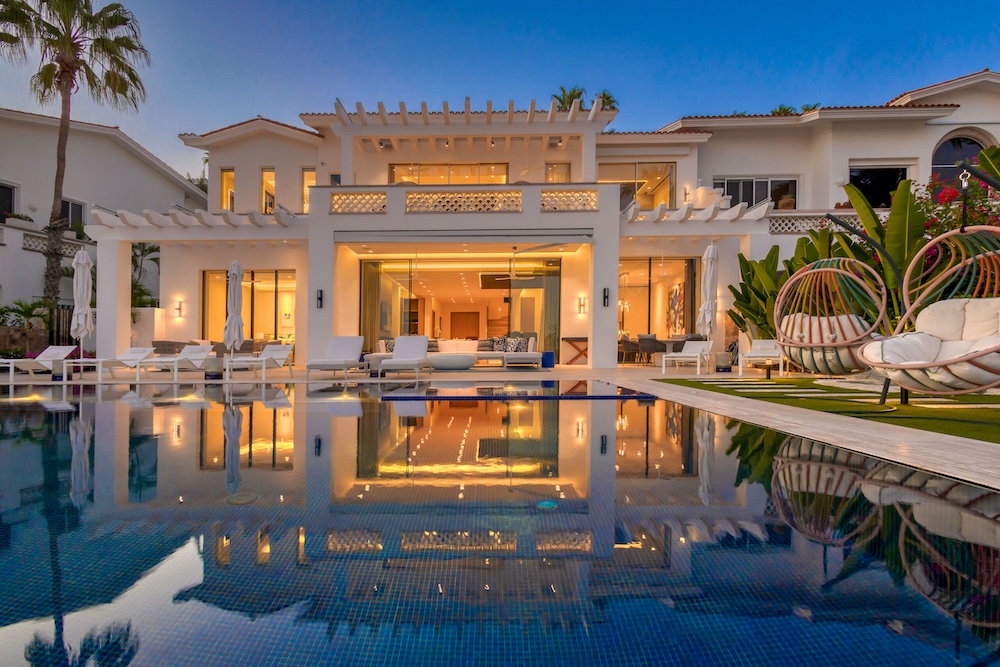 Coldwell Banker Mexico showcases a modern Mexican villa surrounded by palm trees with a clear blue sky in the background.